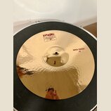Zlatý kovový činel s kladeným povrchem. Na povrchu jsou červené nápisy „Paiste 2002“, „TRADE MARK MADE IN SWITZERLAND“ a „WILD CRASH 19"“. Povrch je…