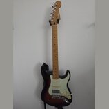 Elektrická kytara s tmele s gradací barvy od černé k hnědé a krčkem ze světlého dřeva. Na hlavě je viditelné logo Fender. Kytara má bílý pickguard, t…