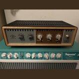 Na fotografii je stolní audio zařízení s černým perforovaným krytem a dřevěným rámem. Na levé straně je logo UA a nápis UNIVERSAL AUDIO, vpravo nápis…
