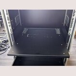 Fotografie znázorňuje otevřený černý rackový case s hliníkovými profily a kovovými lištami pro montáž zařízení. Uvnitř je umístěna jedna černá vysouv…