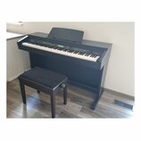 Digitální piano s černým povrchem a přiloženou černou stolečkou s čalouněným sedákem. Na pravé straně nad klávesami je bílý nápis DP330. Nástroj je v…