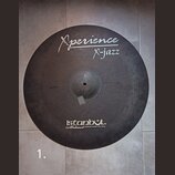 Kulatý činel s tmavým, matným povrchem. Na horní části je bílý nápis „Xperience“ a pod ním „X-jazz“, vlevo od něj je menší nečitelný text. Ve spodní…