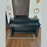 Černý digitální piano v kompaktním provedení s integrovaným stojanem. Nástroj má matný povrch a v dolní části jsou umístěny tři pedály. Na viditelnýc…