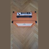 Kytarový kombozesilovač v oranžovém vinylu s černými plastovými rohy a úchytem. Na horním ovládacím panelu je bílý nápis ORANGE CRUSH 20 a řada ovlád…