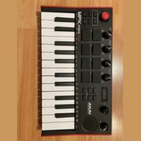 Černý kompaktní MIDI kontrolér s červeným rámem. Na horní části je nápis MPK mini play a v dolní části logo AKAI PROFESSIONAL. Nástroj obsahuje kláve…