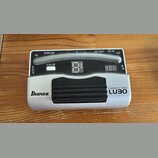 Stříbrný chromatický tuner s černým gumovým pedálem. Na zařízení jsou nápisy Ibanez, CHROMATIC TUNER a LUBO. Horní část obsahuje displej s označením…