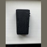 Černý obdélníkový efekt pedál z plastového nebo kovového materiálu s žebrovaným povrchem. Na levé straně je svisle vyražen nápis AMPLIFIER a na pravé…