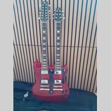 Červená elektrická kytara s dvěma hmaty a dvěma hlavami. Na obou hlavách je bílý nápis Gear4music. Nástroj má dva humbuckery, stříbrný hardware a čer…
