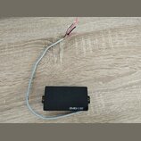 Černý elektrický snímač s obdélníkovým tvarem a dvěma montážními šrouby po stranách. Na spodní hraně je bílý nápis EMG-ESP. Ze snímače vede šedý kabe…