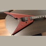 Elektrokytara s červeným matným povrchem v ostrém, atypickém tvaru. Je vybavena dvěma černými humbuckery a černým tremolo mostem. Na těle se nachází…