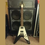 Černá elektrická kytara s bílým pickguardem a Flying V tvarem těla. Na hlavě je viditelné logo "Gibson". Na spodní části těla je nápis "Epiphone". Ky…