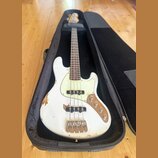 Bílá elektrická basová kytara v černém obalu. Nástroj má světlý hmatník, bílý pickguard a čtyři struny. Povrch bílého trupu vykazuje výrazné opotřebe…
