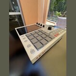 Bíle provedený sampler s mřížkou 16 šedých padů a displejem v horní části. Na spodní hraně je červený nápis AKAI a vedle něj nečitelný text. Zařízení…