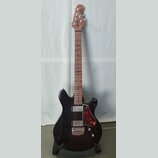 Černá elektrická kytara s tmavě hnědým hnedem hmatníkem a dřevěnou hlavou. Na hlavě je viditelné logo "Cort". Kytara má dva humbuckery, červeně vzoro…