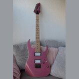 Elektrická kytara s růžovým třpytivým povrchem a světlým hnedým hnedým hmatníkem. Na hlavě je viditelný nápis Danelectro. Nástroj má dva snímače typu…