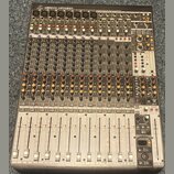 Šedý mixovací pult s mnoha ovládacími prvky, posuvníky a konektory. V horní části je nápis Behringer XENYX UFX1604. Povrch přístroje vykazuje mírné z…