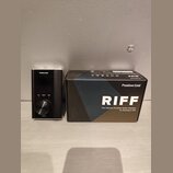 Černý přenosný kytarový interface s kovovým povrchem a velkým ovládacím knoflíkem. Na zařízení jsou nápisy Positive Grid, RIFF a označení CLIP, DIREC…