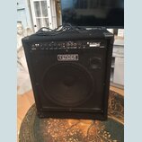Černý basový kombozesilovač s mřížkou před reproduktorem. Na horním ovládacím panelu je nápis RUMBLE 100 a na přední mřížce logo FENDER BASS AMPLIFIC…