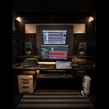 Fotografie zachycuje kompletní studio s pracovním stolem z tmavého dřeva. Na stole jsou dva počítačové monitory s otevřeným softwarem pro nahrávání,…