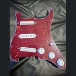 Vinylový pickguard v tmavě červené barvě s texturou želvy, osazený třemi bílými snímači. Na ovládacích knoflících jsou nápisy VOLUME, TOINE a ONE. So…