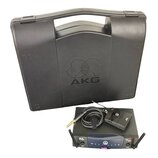 Černý plastový kufřík s vyraženým logem AKG. Před ním je umístěn bezdrátový přijímač s nápisy SR 40 a AKG Wireless System, vysílač s logem AKG a kabe…