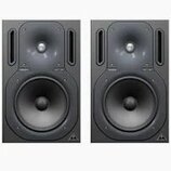 Dva černé studiové monitory s membránami a výšk SPEAKERY. V pravém dolním rohu každého reproduktoru je bílé trojúhelníkové logo. Povrch je matně čern…