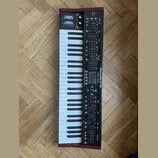 Černý syntetizátor s klávesnicí a dřevěnými bočními panely. Na přístroji je bílý nápis DeepMind 12 a logo Behringer. Ovládací panel obsahuje zahlreic…