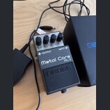 Kytarový efekt pedál stříbrné a černé barvy. Na horní části je nápis Metal Core ML-2 a logo boss. Pedál má čtyři ovládací knoflíky s popisky MIN a MA…