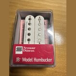 Dvě bílé snímače typu humbucker v průhledném plastovém obalu. Na levém snímači je svisle napsáno Seymour Duncan. Před nimi je červený štítek s logem…