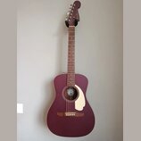 Akustická kytara v matové vínové barvě s krémovým pickguardem. Na hlavě hmatníku je bílý nápis Fender. Uvnitř ozvučovacího otvoru je vidět štítek s l…