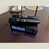 Sada bezdrátových mikrofonů tvořená dvěma černými ručními mikrofony a černým přijímačem se dvěma anténami. Na předním panelu přijímače je digitální d…