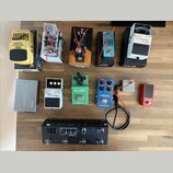 Fotografie zobrazuje sadu kytarových efektů a příslušenství na dřevěném povrchu. V horní řadě jsou pedály Graphic Equalizer EQ700, TONEX a Boss Chrom…