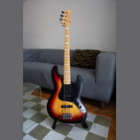Elektrická basová kytara s trupem v barevném přechodu od žluté přes oranžovou k červené a černé. Nástroj má černý pickguard, javorový hmatník a světl…