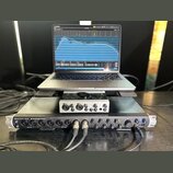 Fotografie zachycuje stoh elektronického vybavení složený z notebooku, malého efektového pedálu a zvukové karty. Vepředu je stříbrná zvuková karta s…