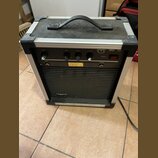 Kytarový kombozesilovač v hliníkovém flightcase s černým povrchem a úchytem. Na horním ovládacím panelu jsou čtyři černé otočné ovladače s popisky GA…