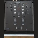 Černý DJ mixér značky Numark s označením M2 v levém dolním rohu. Přístroj obsahuje řadu otočných knoflíků pro ovládání GAIN, TREBLE, MID a BASS, cent…