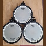 Tři elektronické bicí pady značky Roland v černé barvě s bílými okraji. Na každém padu je nápis „Roland“, pod ním text „MESH HEAD“ a „Reg. U.S. Pat.…
