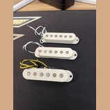 Tři elektrické snímače typu single-coil v bílém plastovém provedení. Každý snímač má šest viditelných kovových pólů a připojovací vodiče v různých ba…