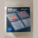 Fotografie znázorňuje krabici od efektového procesoru s nápisy B1on a Bass Multi-Effects Processor. V pravém horním rohu je logo ZOOM. Na obrázku pří…