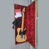 Elektrická kytara typu Telecaster v přírodní dřevěné barvě s černým pickguardem, umístěná v otevřeném kufru s červeným plyšovým vnitřkem. Na hlavě hm…