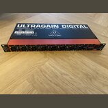 Černý rackový audio interface s červeným horním panelem. Na spodní straně je nápis ULTRAGAIN DIGITAL AUDIOPHILE 8 IN/8 OUT ADAT AUDIO INTERFACE MODEL…