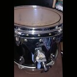 Černý buben s chromovaným obručováním a kováním. Na chromovaném kotevním mechanismu je viditelné logo Gretsch. Povrch blány vykazuje známky opotřeben…