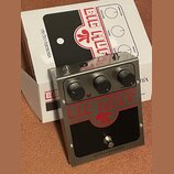Kytarový efekt pedál v kovovém stříbrném šasi s černým panelem. Na pedálu je červený nápis BIG MUFF a v dolní části černý nápis electro-harmonix. Zař…