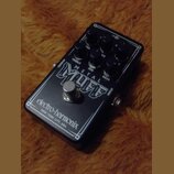 Černý efekt pedál s bílým vymezením hran a nápisy. Na horní části jsou čtyři ovládací knoflíky s popisky VOL, TREBLE, MID a BASS. Uprostřed je velký…