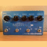 Modrý efekt pedál s nápisem FLASHBACK X4 a logem tc electronic. Zařízení má čtyři černé ovládací knoflíky s popisky TONEPRINT, DELAY TIME, FEEDBACK,…