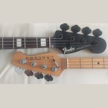 Fotografie zachycuje hlavy dvou basových kytar. Horní je černá s nápisy Fender, DELUXE JAZZ BASS SPECIAL, MADE IN MEXICO a sériovým číslem MXD1901226…
