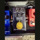 Černý efekt pedál s nápisy MXR, BASSINNOVATIONS a envelope filter. Na horní části jsou čtyři ovládací knoflíky s popisky DRY, FX, DECAY a SENS, upros…