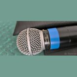 Detailní pohled na dynamický mikrofon s černým tělem a modrým kroužkem. Na stříbrném prstenci pod mřížkou je černý nápis SM58 DYNAMIC. Kovová mřížka…