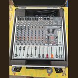 Stříbrný mixážní pult značky behringer, model XENYX X1222USB. Zařízení je umístěno v ochranném černém kufru s pěnovou výplní. Na panelu jsou vidět po…
