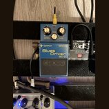 Modrý efekt pedál s nápisy Blues Driver a BD-2. Na spodní části je viditelné logo BOSS. Pedál má tři ovládací knoflíky s popisky LEVEL, TONE a GAIN a…